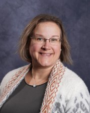 Catherine Griffin, Board President. Female with dark blonde hair and glasses smiling for headshot on a gray background